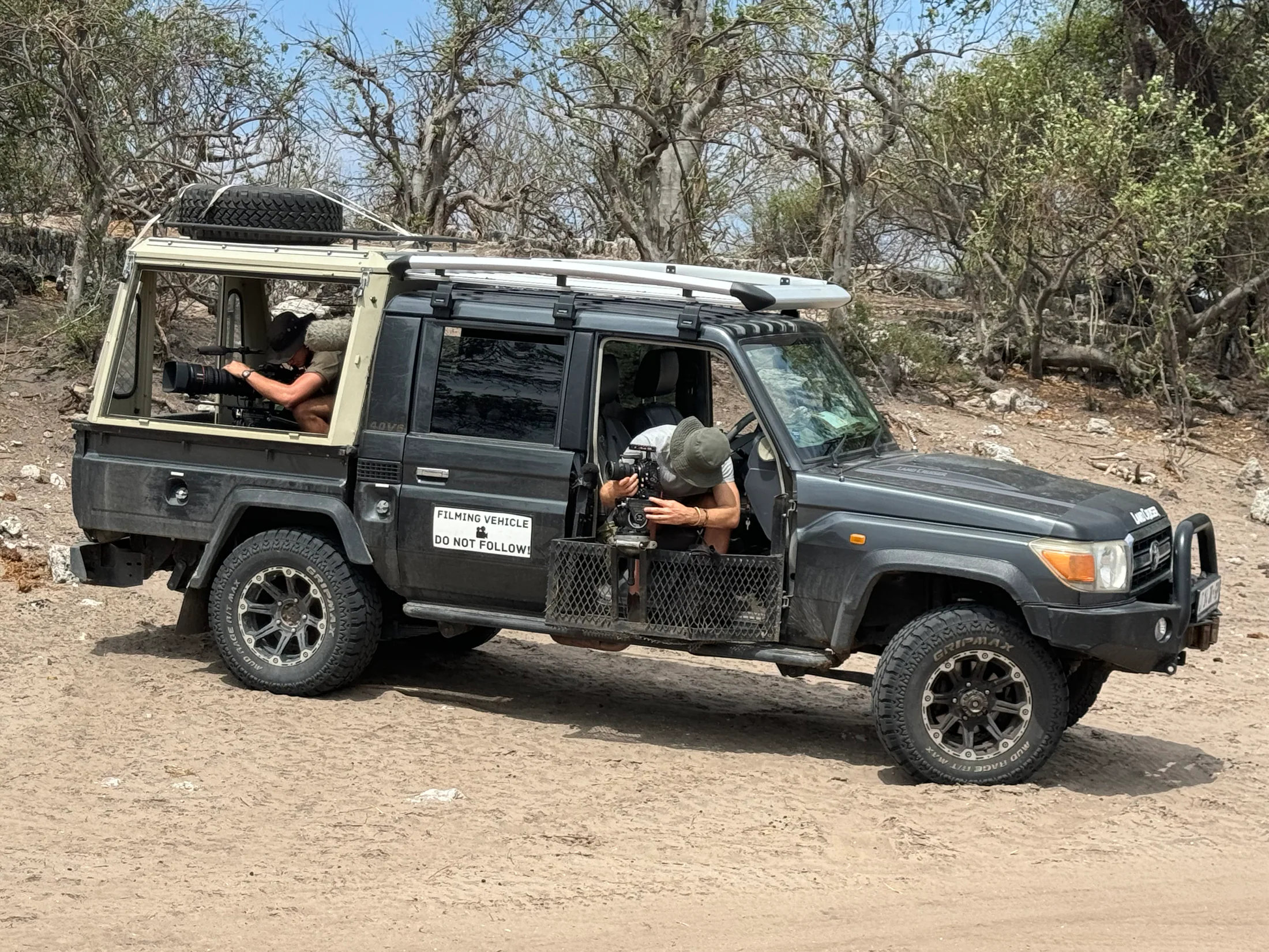 Two camera operators filming from a field vehicle